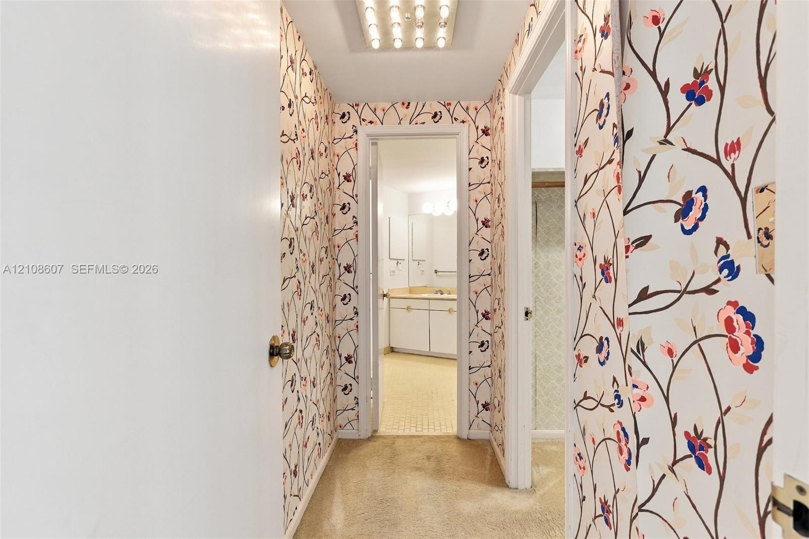 Hallway featuring floral-patterned wallpaper, flush-mount lighting, and solid-core interior doors with metallic hardware