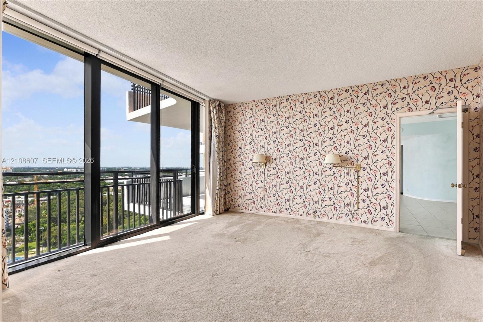 Floor-to-ceiling windows, private balcony access, wall-mounted light fixtures, and patterned wallpaper