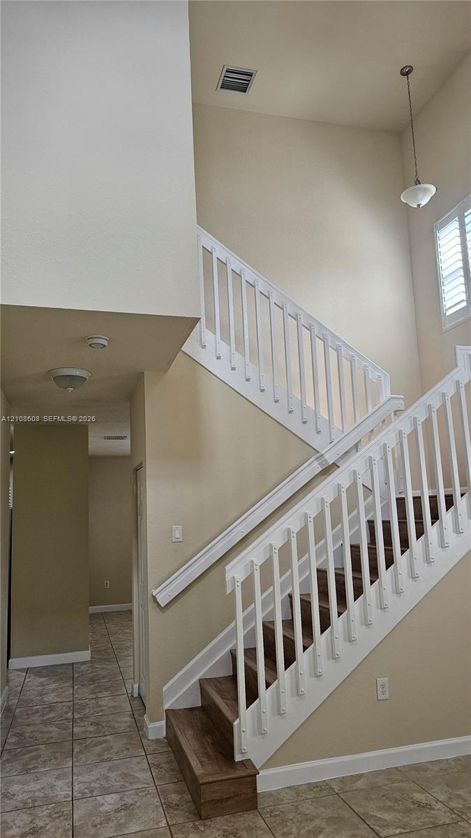 Staircase featuring wood-finish treads, white balusters, high ceilings, tile flooring, and a pendant light fixture
