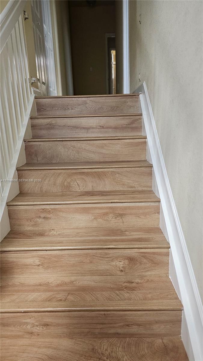 Staircase featuring wood-finish flooring treads and white painted handrails with matching vertical balusters