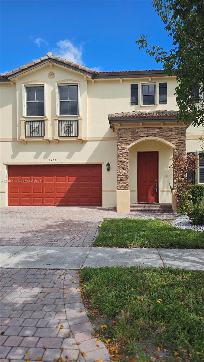 Two-story exterior featuring stucco siding, decorative stone masonry at the entryway, a paver driveway, arched entryway, and metal Juliet balcony railings Two-story exterior featuring stucco siding, decorative stone masonry at the entryway, a paver driveway, arched entryway, and metal Juliet balcony railings