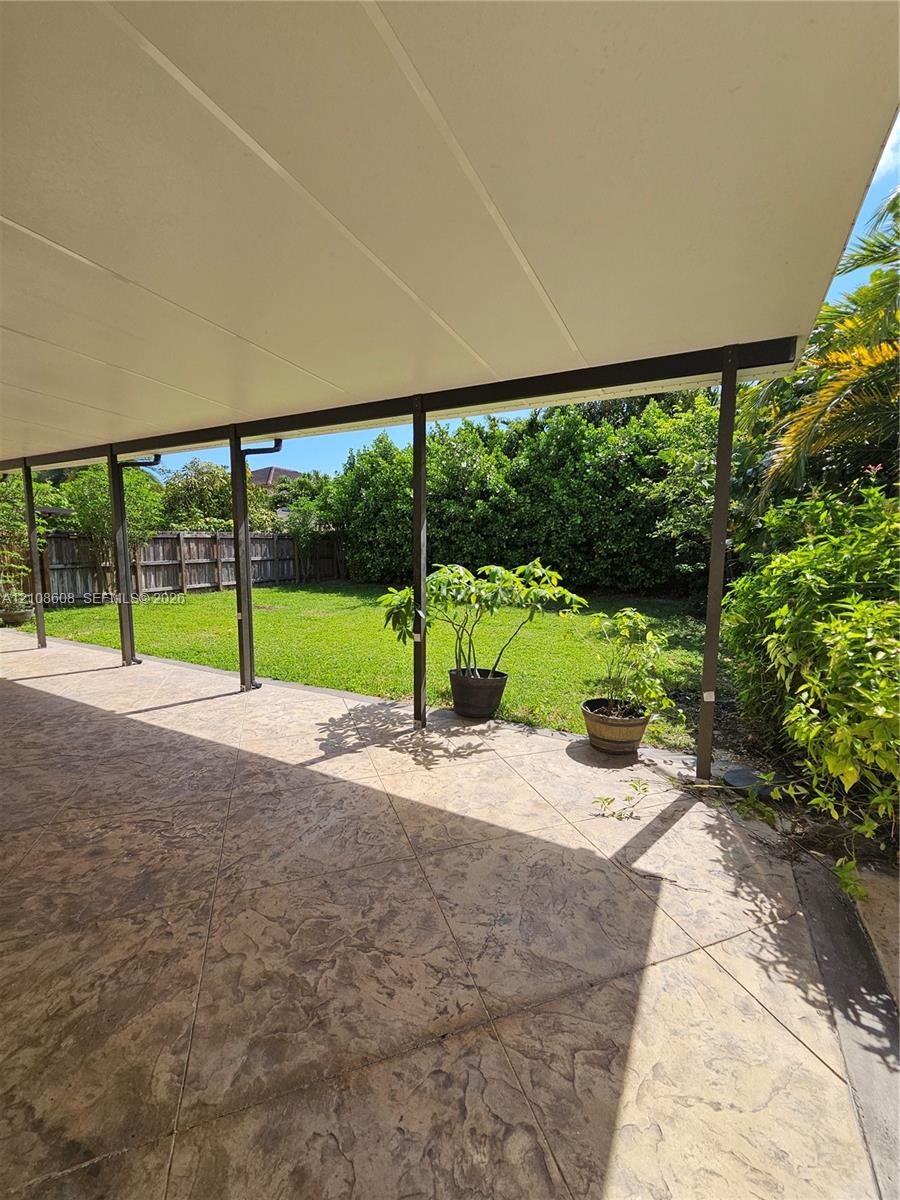 Covered patio with stamped concrete flooring, grass lawn, and perimeter wood fencing