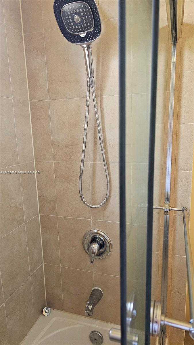 Bathtub and shower combination featuring square-profile rain shower head with adjustable hand-held wand, chrome finish fixtures, glass enclosure, and neutral-tone wall tile