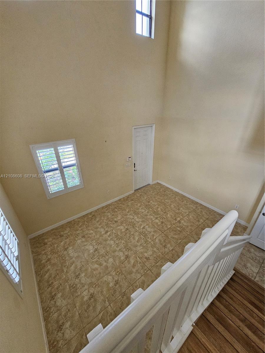 Double-height ceiling featuring tall vertical windows, tile flooring, and a white wood-finish staircase railing