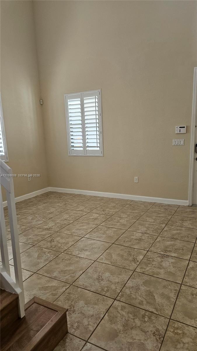 High-ceiling interior featuring tiled flooring, plantation shutters, and a wood-finish staircase railing
