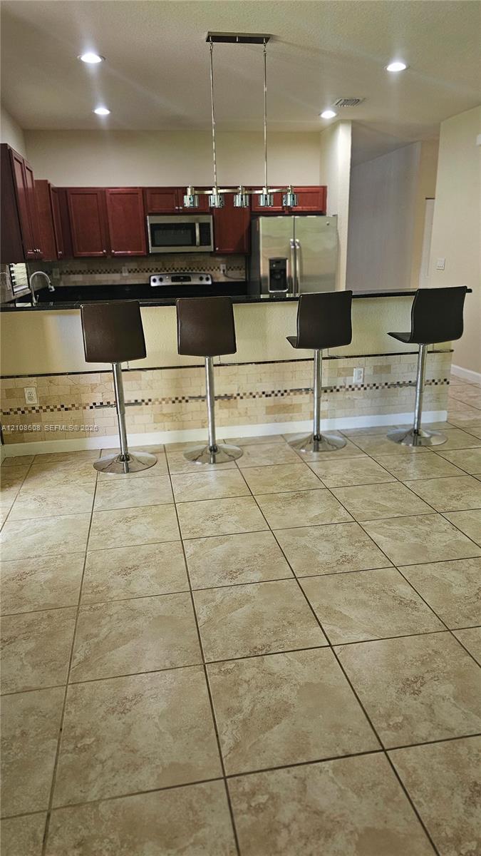 Kitchen featuring a peninsula island, stainless steel appliances, tile flooring, stone-tiled backsplash, and overhead pendant lighting