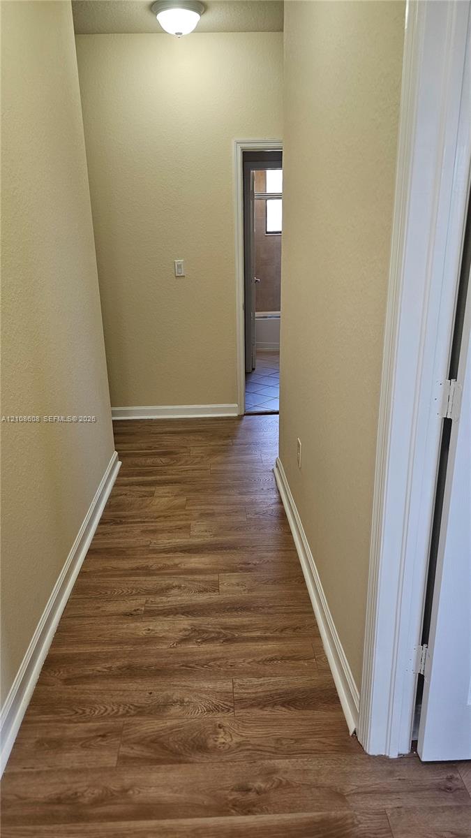 Hallway featuring wood-finish flooring, neutral-toned walls, and a flush-mount ceiling light fixture
