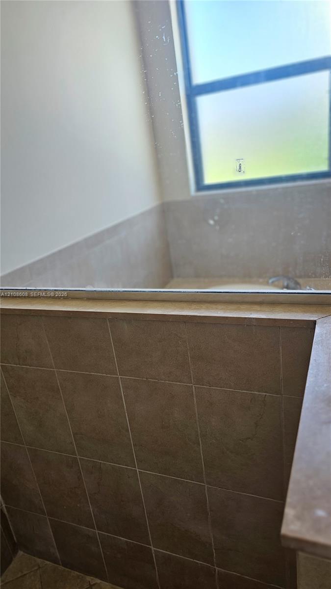 Soaking tub featuring a tiled surround, a neutral-toned stone ledge, and a large window
