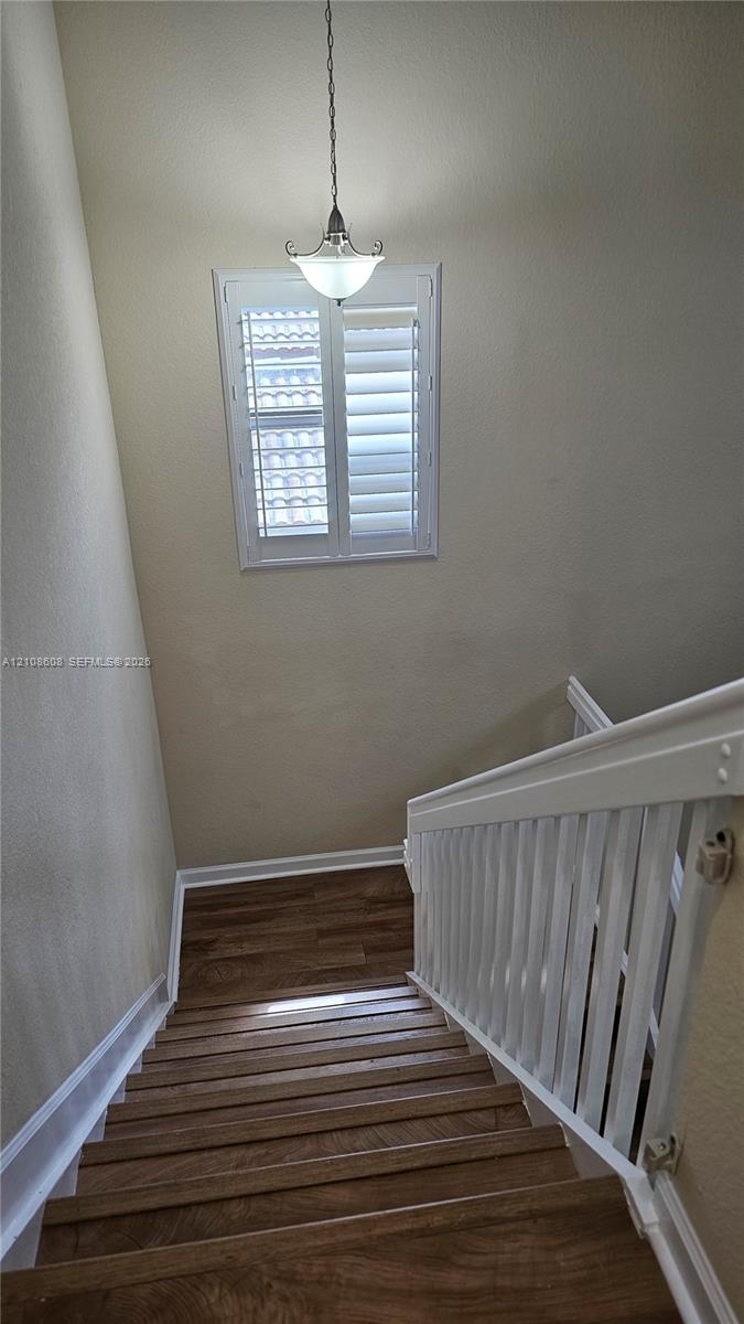 Staircase featuring wood-finish treads, a white balustrade, a window with interior shutters, and a pendant light fixture