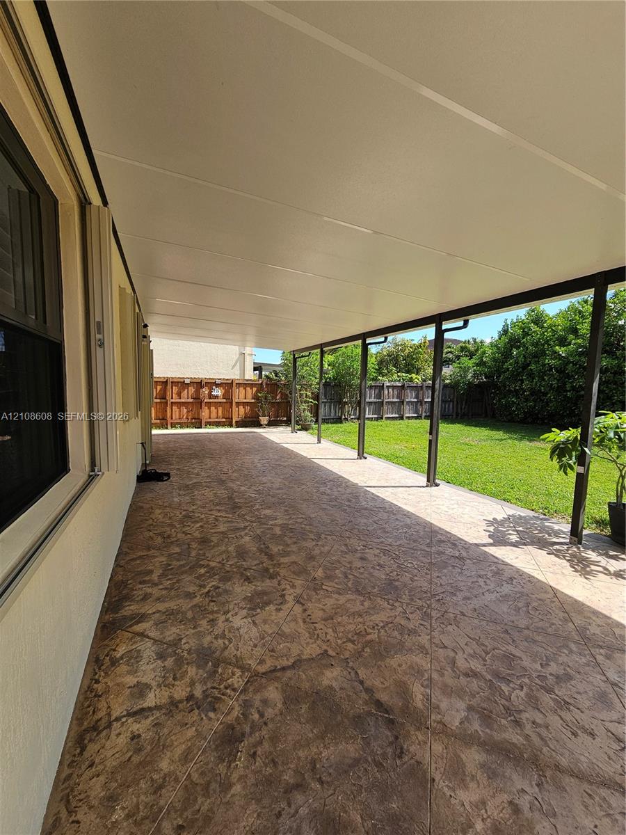 Covered patio featuring stamped concrete flooring, support columns, and a grassy backyard enclosed by wooden fencing