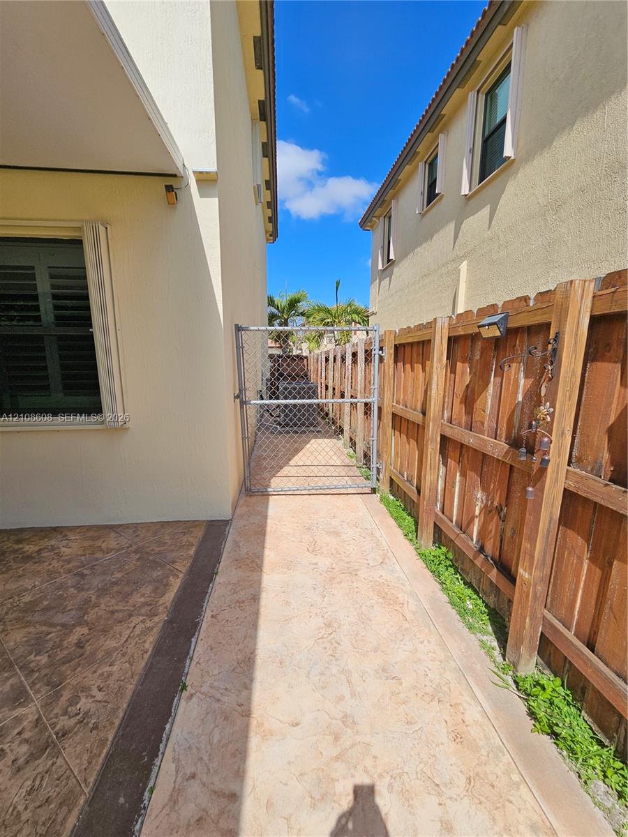 Side yard featuring stamped concrete paving, wood privacy fencing, and a chain-link gated access point