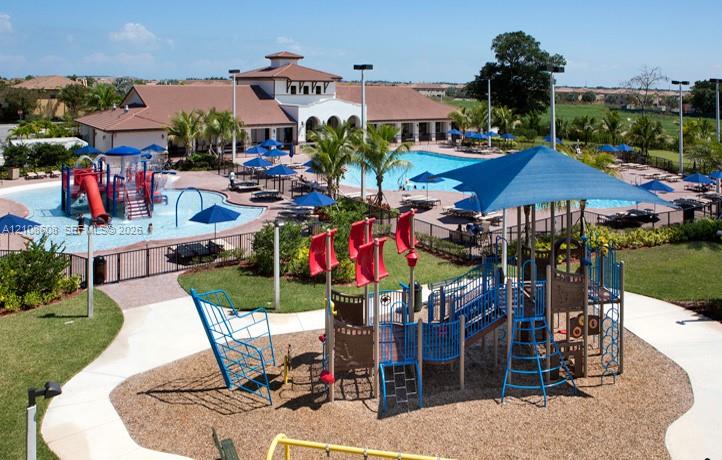Community recreation area featuring an expansive swimming pool, a splash pad with water features, a shaded jungle gym, and a clubhouse facility