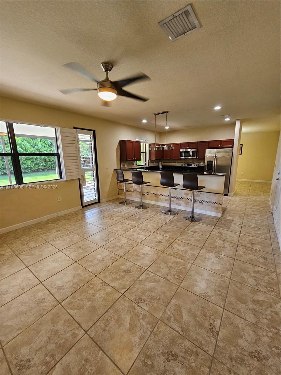 Kitchen featuring dark wood cabinetry, a stone-accented breakfast bar, stainless steel appliances, large-format tile flooring, and a ceiling fan
