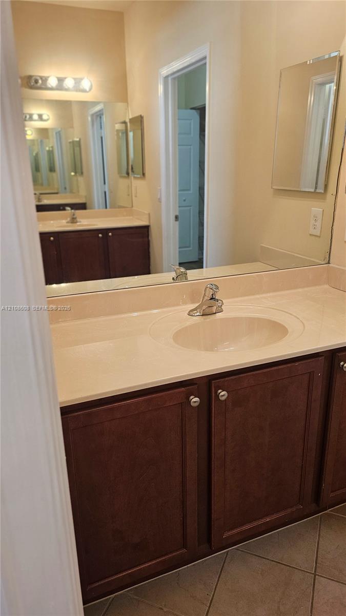 Vanity featuring dark wood cabinetry, an integrated basin, a neutral-toned countertop, a multi-bulb light fixture, and a large-format mirror