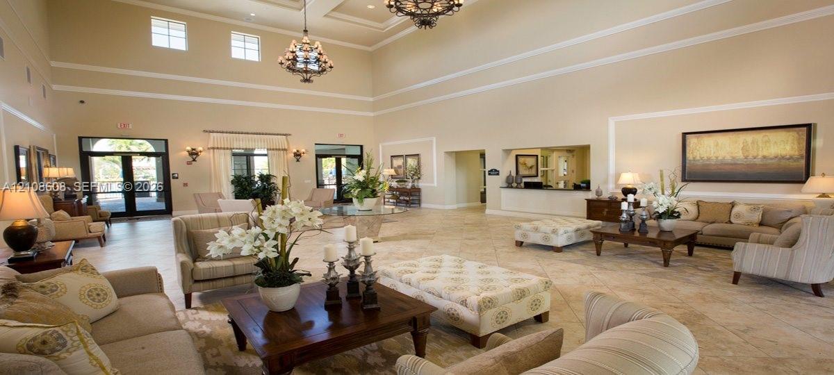 Expansive room featuring soaring ceilings, multi-tier chandeliers, stone-finish tile flooring, recessed crown molding, and a service counter with built-in cabinetry