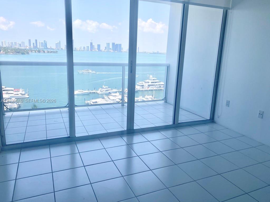 Floor-to-ceiling sliding glass doors, white ceramic tile flooring, and a private balcony featuring a glass railing Floor-to-ceiling sliding glass doors, white ceramic tile flooring, and a private balcony featuring a glass railing
