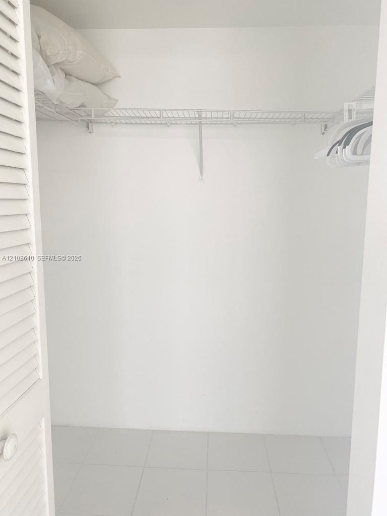 Closet featuring white louvered doors, wire shelving, and tile flooring Closet featuring white louvered doors, wire shelving, and tile flooring