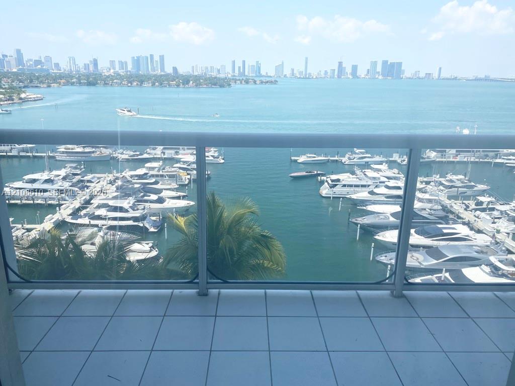 Private balcony featuring white tile flooring and a glass-paneled railing, overlooking a marina and city skyline Private balcony featuring white tile flooring and a glass-paneled railing, overlooking a marina and city skyline