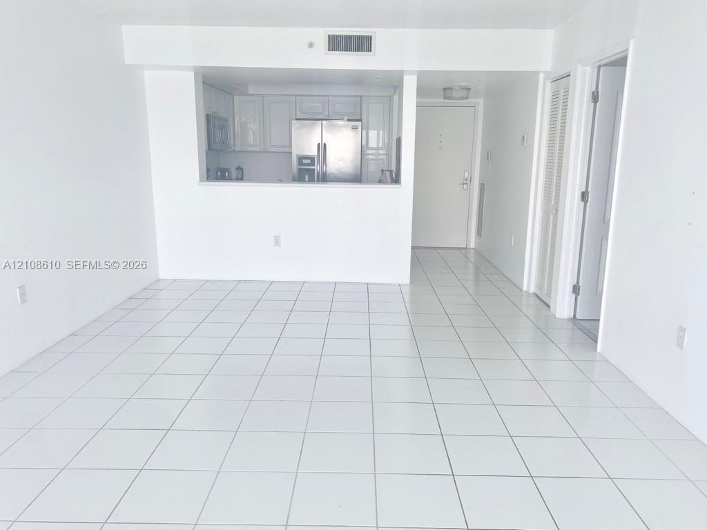 Open-concept interior featuring white ceramic floor tiling, white cabinetry, stainless steel kitchen appliances, and bi-fold closet doors Open-concept interior featuring white ceramic floor tiling, white cabinetry, stainless steel kitchen appliances, and bi-fold closet doors