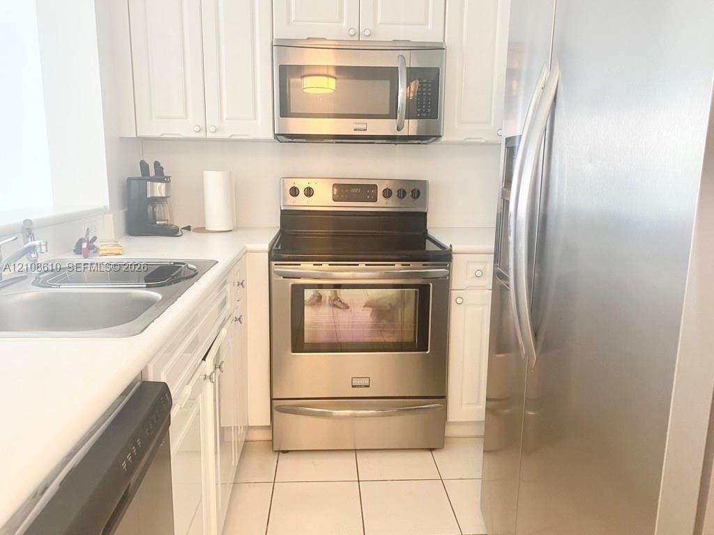 Kitchen featuring white cabinetry, stainless steel appliances, a glass-top electric range, a built-in microwave, and tile flooring Kitchen featuring white cabinetry, stainless steel appliances, a glass-top electric range, a built-in microwave, and tile flooring