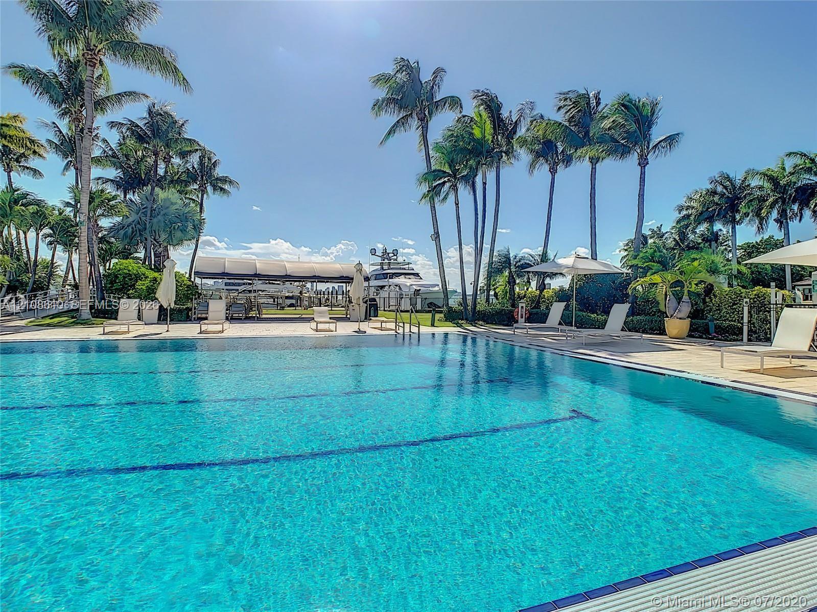 Swimming pool featuring tiled lane markers, stone-paved deck, covered boat dock, and mature palm trees