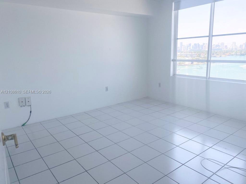 Bright room featuring white ceramic floor tiles, floor-to-ceiling windows, and an expansive cityscape and water horizon