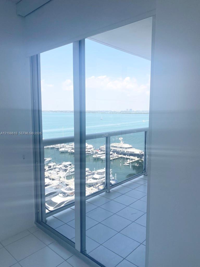 Floor-to-ceiling sliding glass door, private balcony with tiled flooring, and metal railing overlooking the marina