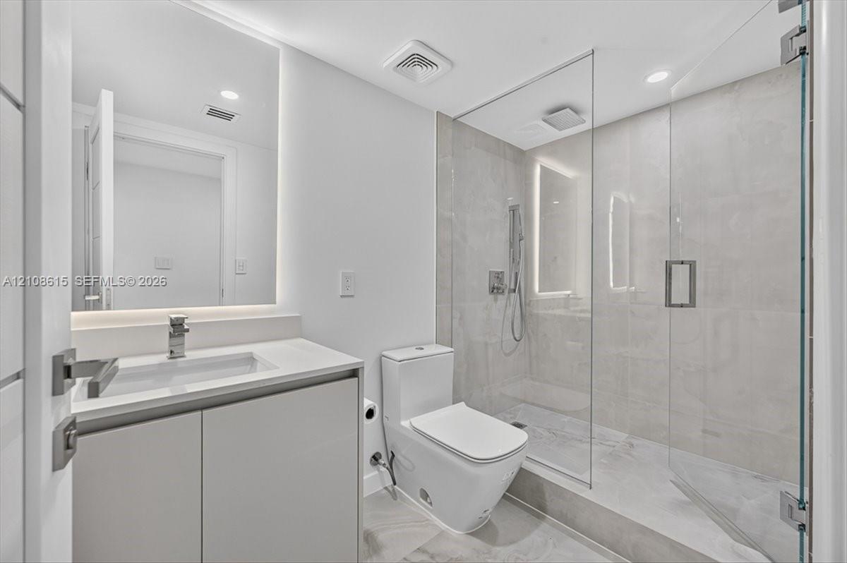 Modern bathroom featuring a floating vanity with a light-toned countertop, a seamless walk-in shower with a glass enclosure, large-format tile flooring, and backlit wall mirror