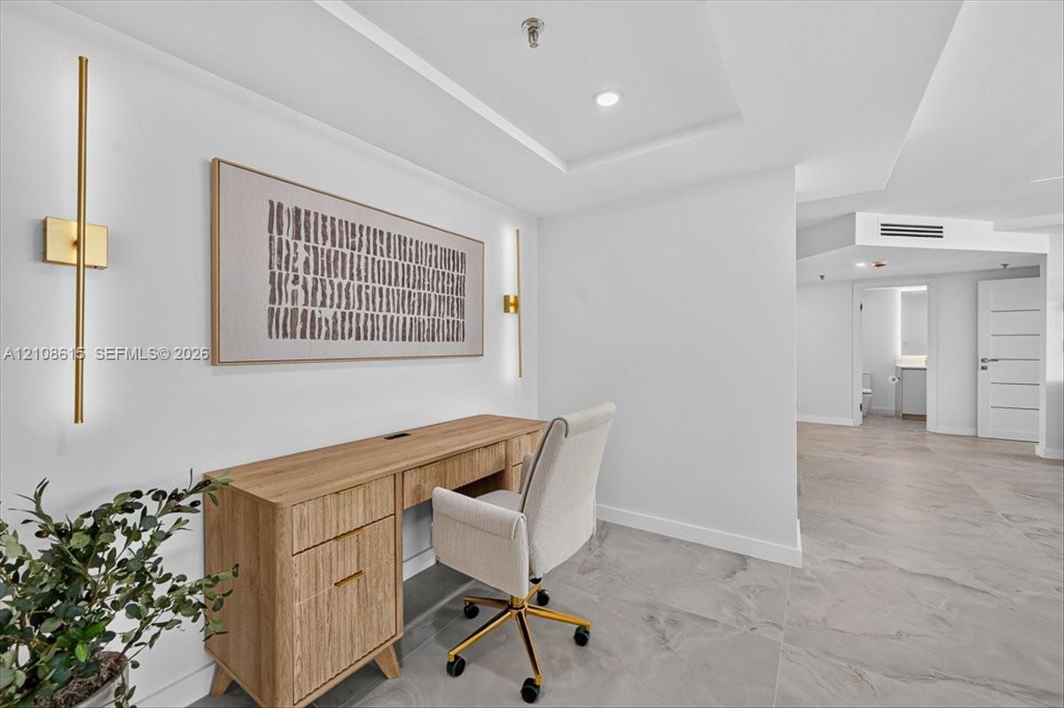 Neutral-toned tile flooring, recessed tray ceiling lighting, and dual vertical gold-tone wall sconces