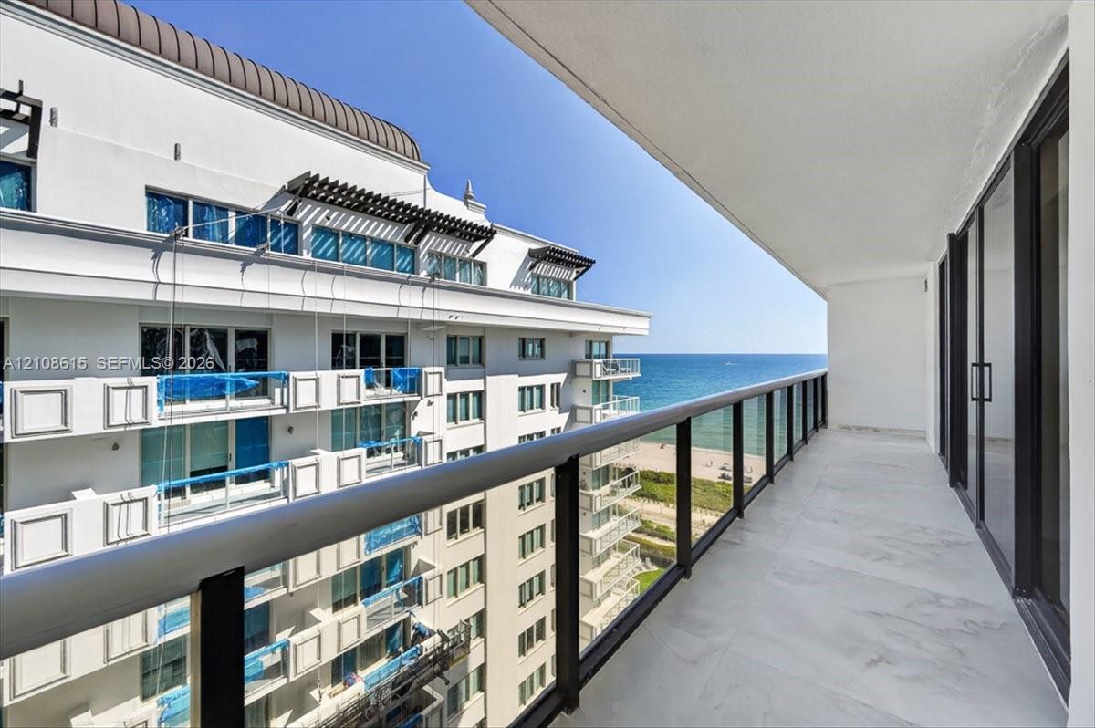 Covered balcony featuring large-format stone-finish tile flooring, sleek dark metal railings with glass panels, and sliding glass door access