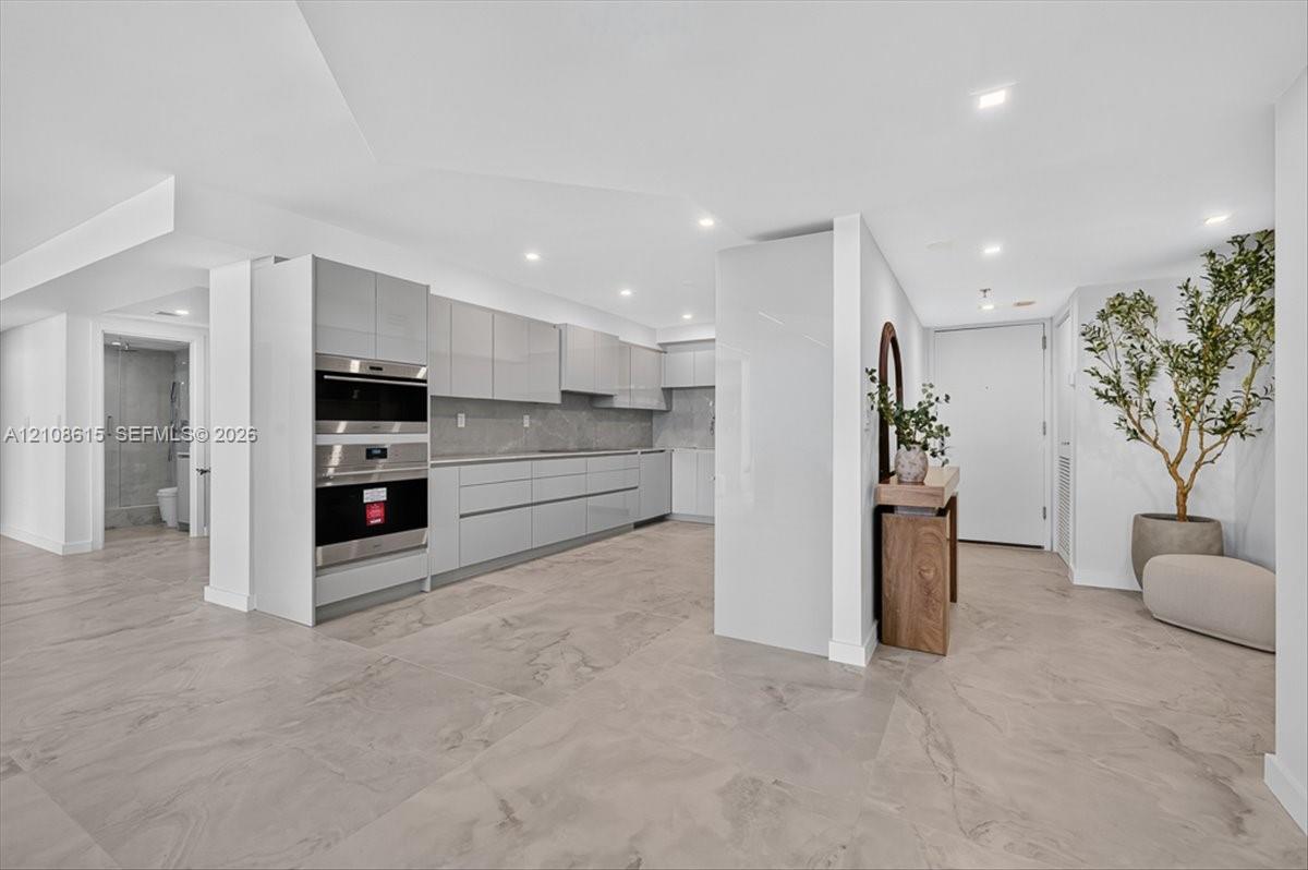 Modern kitchen featuring high-gloss cabinetry, stone-surface countertops, built-in double ovens, and large-format tile flooring with recessed lighting