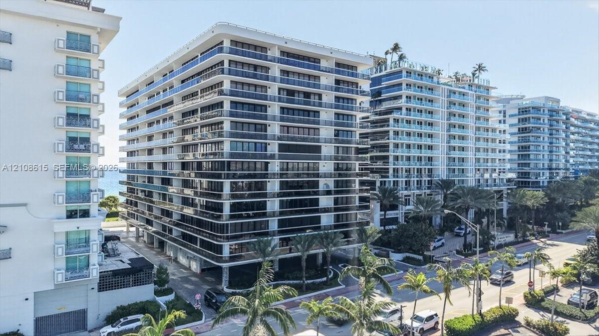 Multi-story residential building featuring glass-railed balconies, a concrete exterior facade, and mature palm tree landscaping