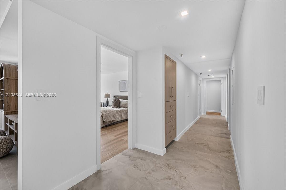 Hallway featuring large-format tile flooring, recessed ceiling lighting, and built-in floor-to-ceiling cabinetry with wood-finish doors