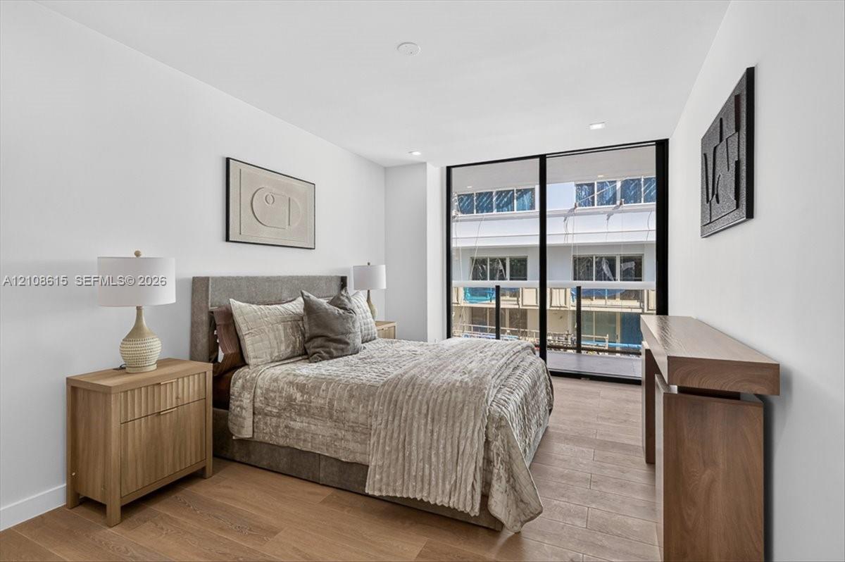 Wood-finish flooring, floor-to-ceiling glass sliding door, integrated recessed lighting, and a private balcony with glass railing