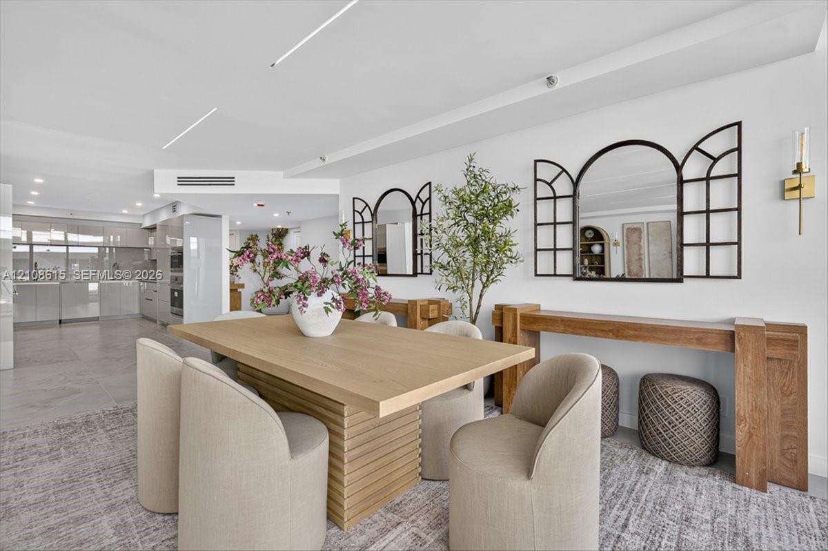 Open-concept living space featuring high-gloss cabinetry, linear recessed lighting, stone-finish flooring, and wall-mounted brass light fixtures