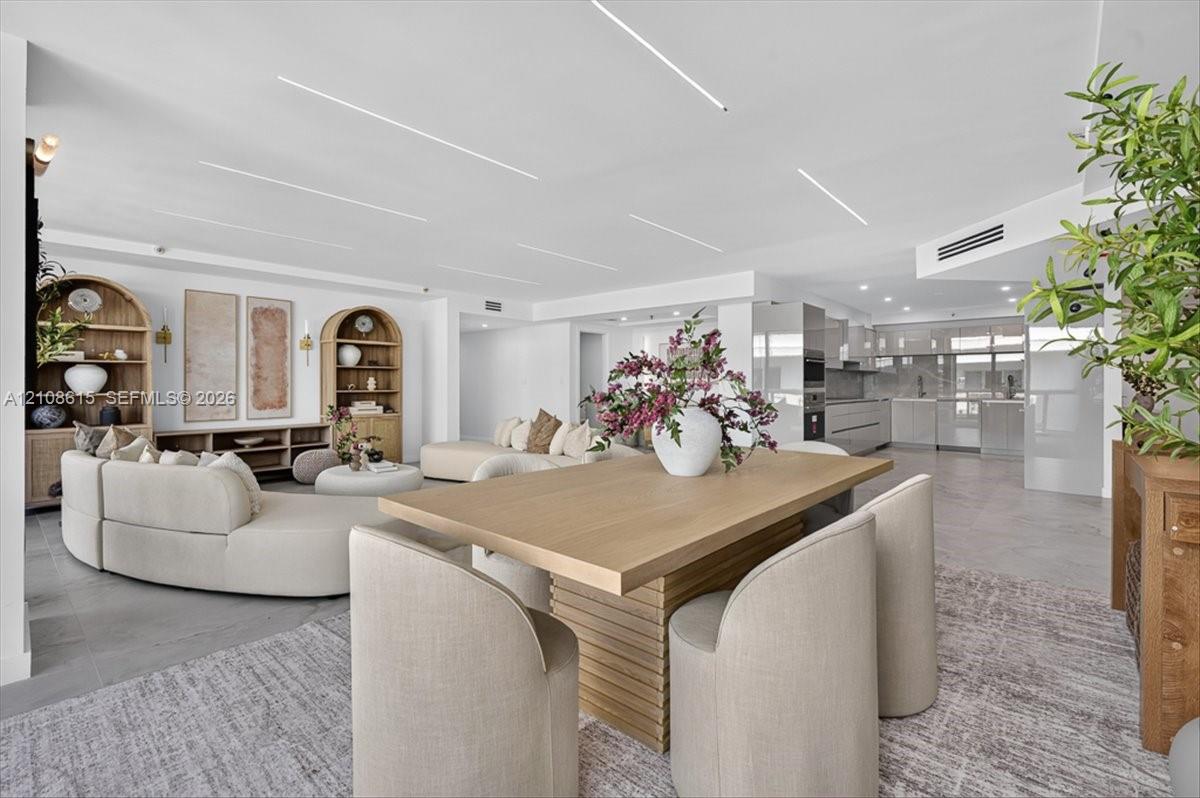 Open-concept interior featuring linear recessed ceiling lighting, built-in arched shelving units, neutral large-format tile flooring, and integrated kitchen cabinetry