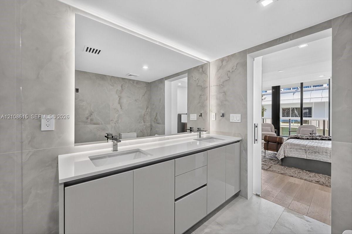 Floating dual-vanity with integrated sinks, quartz countertop, backlit vanity mirror, and floor-to-ceiling stone wall tiling