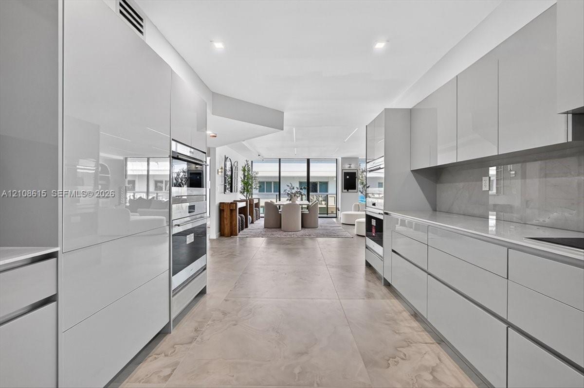 Contemporary kitchen featuring high-gloss cabinetry, large-format tile flooring, stone-surfaced countertops, and built-in stainless steel double ovens
