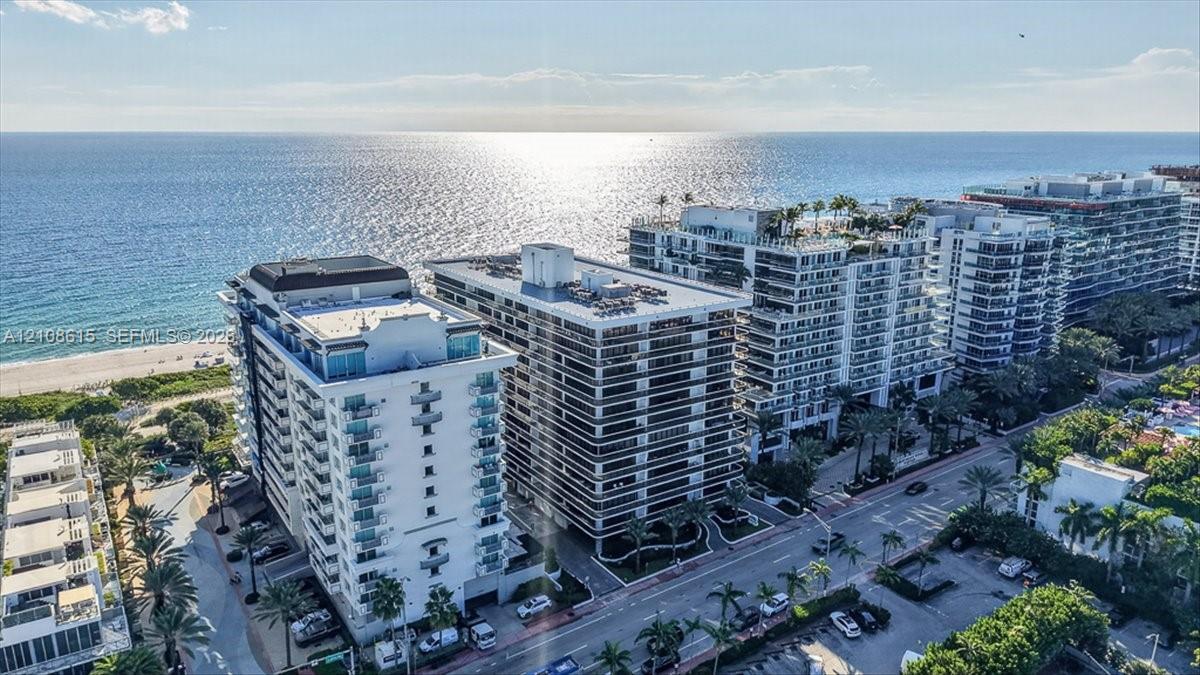 Aerial perspective of coastal high-rise building with glass-railed balconies, exterior masonry facade, and direct proximity to the oceanfront