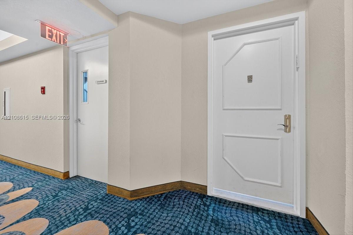 Interior hallway featuring patterned floor covering, smooth wall finishes, and solid-core entry doors with metallic lever hardware
