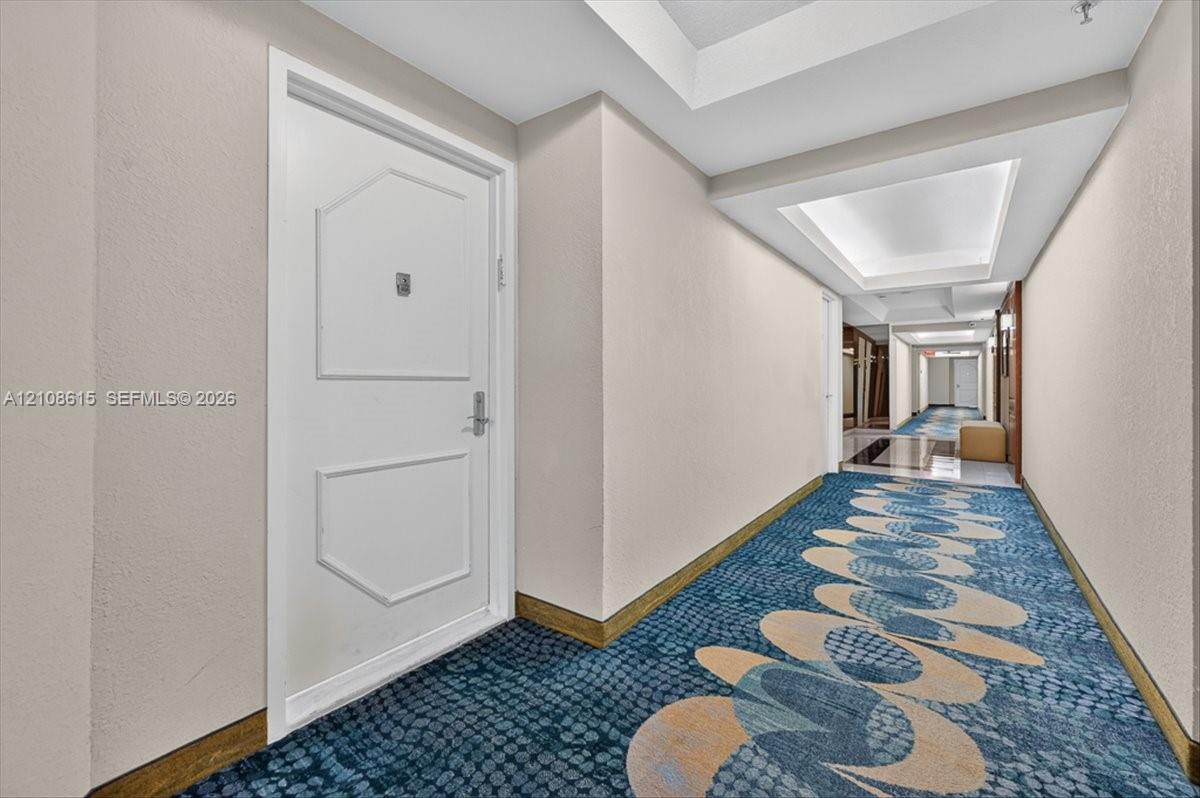 Interior corridor featuring a white paneled door with metal hardware, recessed ceiling lighting, and patterned carpeting
