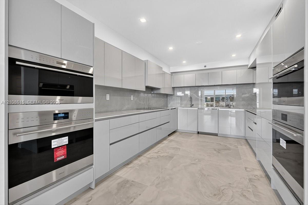Modern kitchen featuring high-gloss cabinetry, stone-finish tile flooring, integrated stainless steel ovens, and recessed lighting