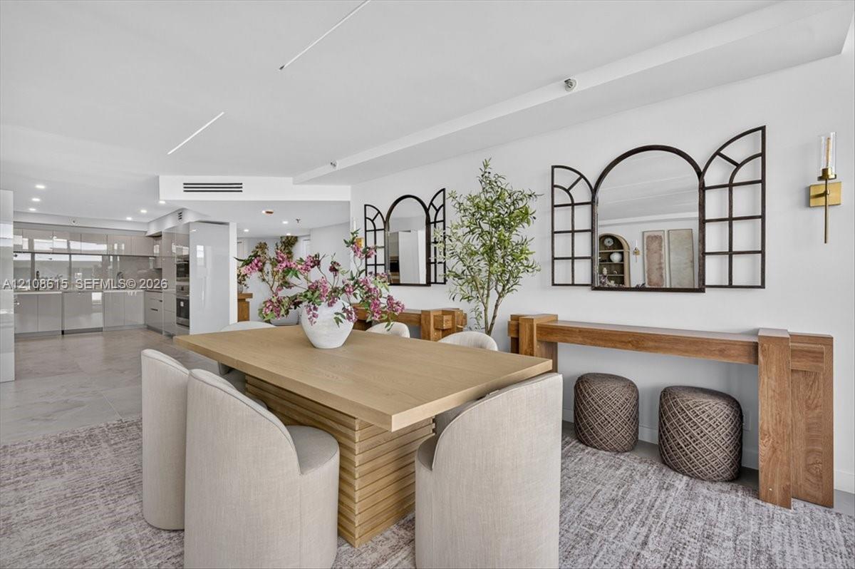 Open-concept interior featuring recessed lighting, sleek cabinetry, neutral tile flooring, and minimalist wall-mounted gold-toned light fixtures