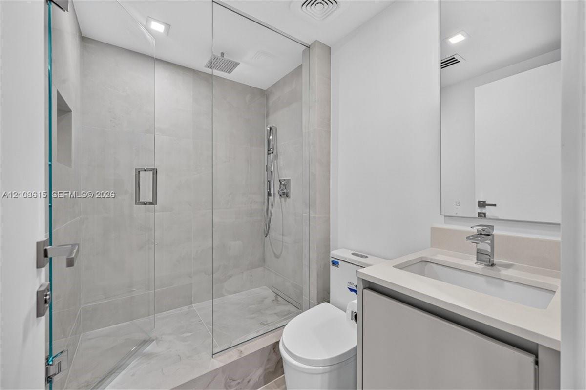 Bathroom featuring a glass-enclosed shower with a rainfall showerhead, large-format tile surround, integrated shower niche, wall-mounted vanity with a rectangular sink, and polished chrome fixtures