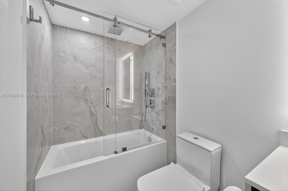 Shower with glass sliding enclosure, floor-to-ceiling stone-finish tile surround, ceiling-mounted rainfall showerhead, and integrated handheld fixture