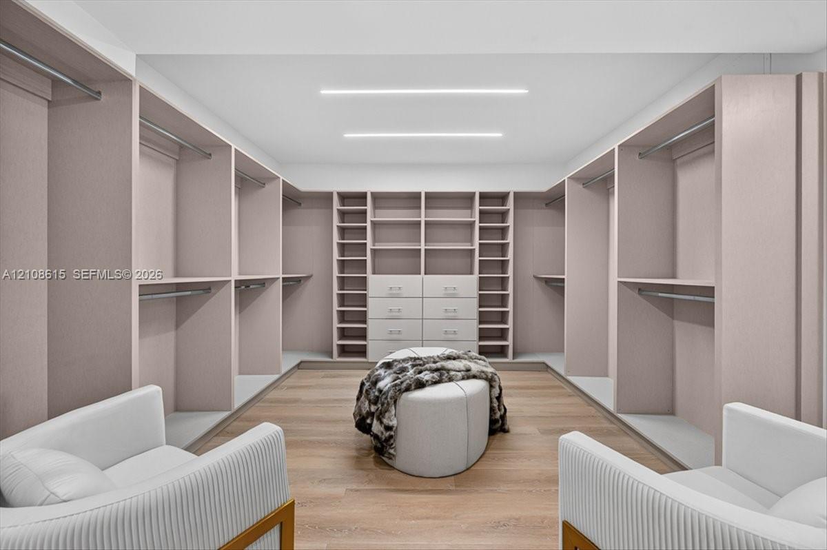 Custom walk-in closet featuring floor-to-ceiling built-in cabinetry, integrated drawer storage, wood-finish flooring, and recessed linear ceiling lighting