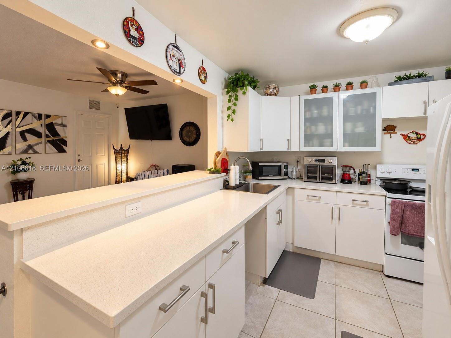 Kitchen featuring white shaker-style cabinetry, quartz countertops, glass-front upper cabinet doors, and tile flooring