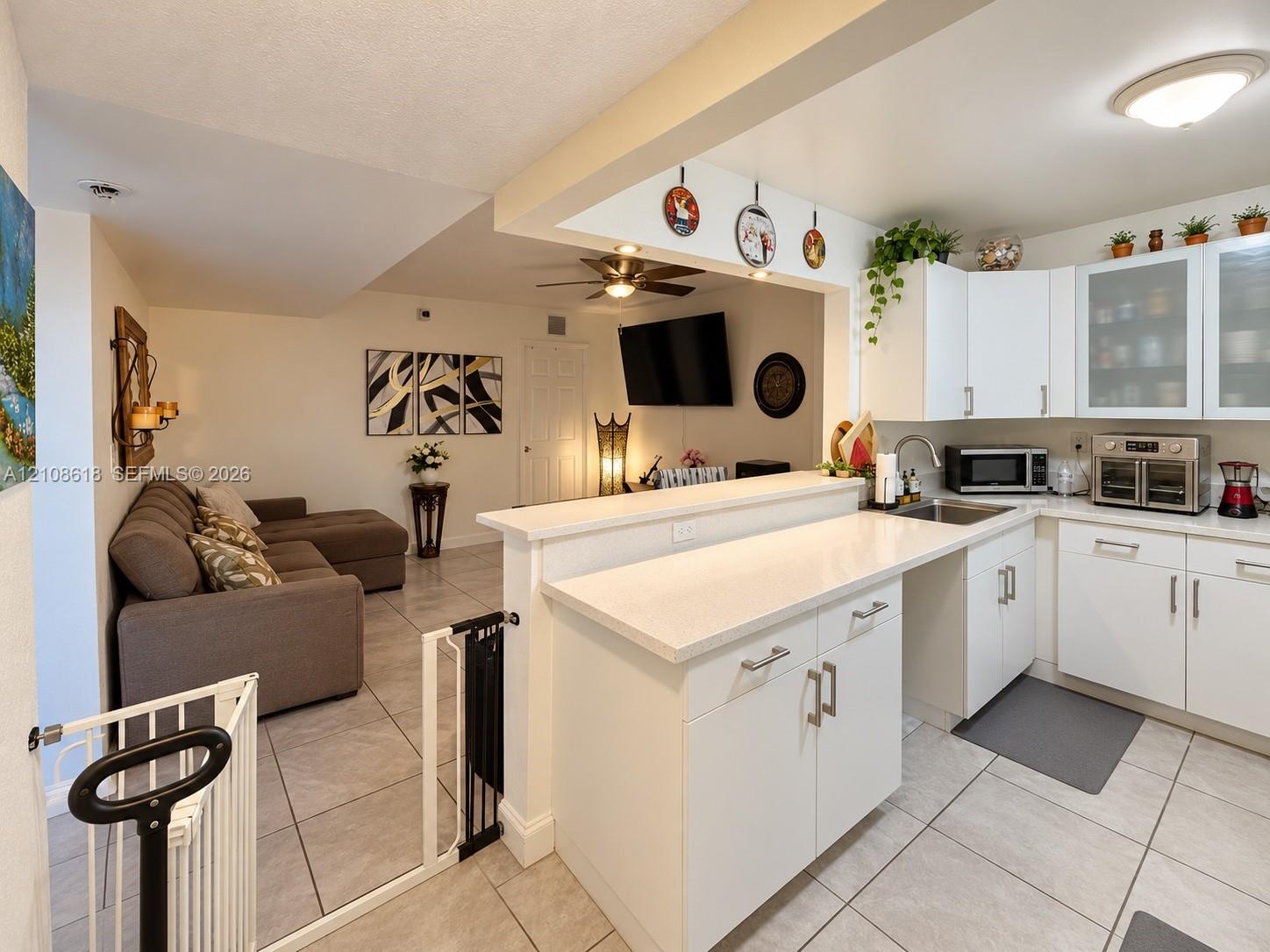 Kitchen featuring white cabinetry with glass-panel upper doors, a stone-finish countertop with breakfast bar, stainless steel sink, and ceramic tile flooring