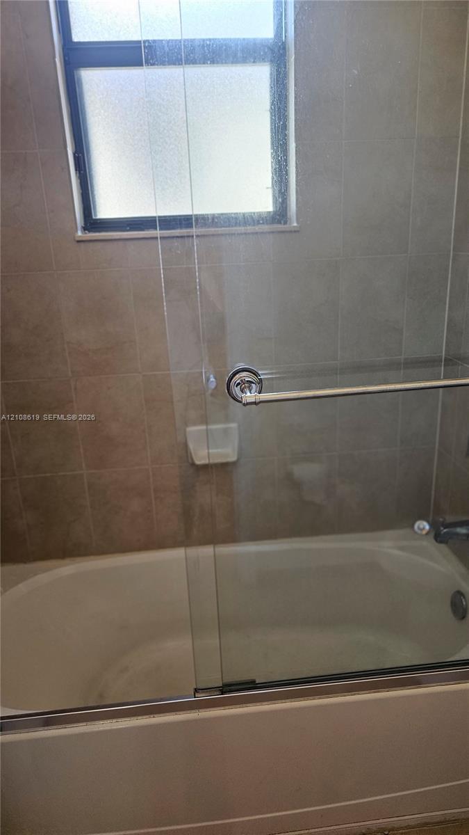 Bathtub with a glass sliding enclosure, integrated soap dish, and neutral wall tile surround