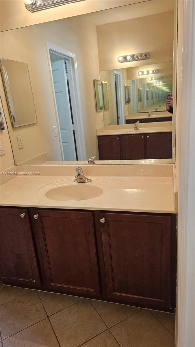 Bathroom vanity featuring wood-finish cabinetry, a solid surface countertop with an integrated basin, a large wall-mounted mirror, and multi-bulb vanity lighting